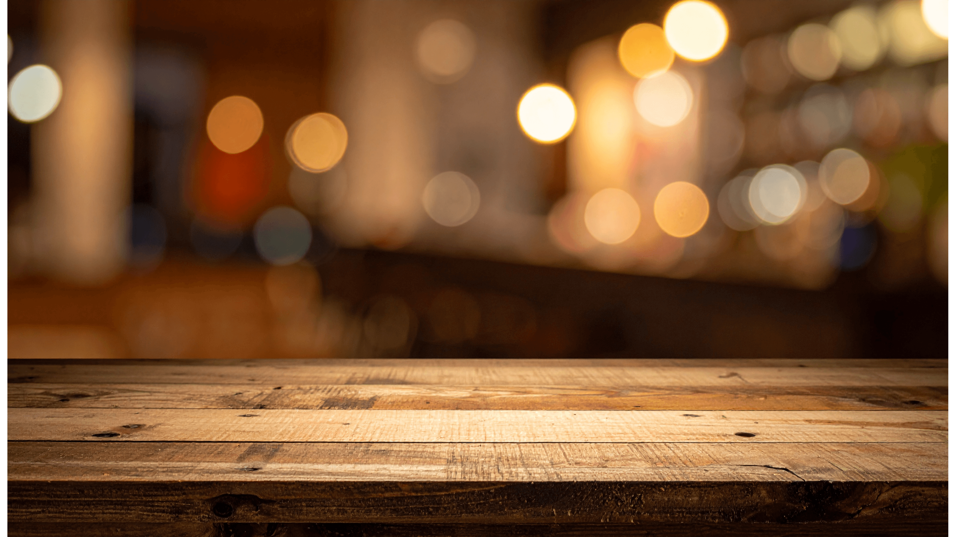 Empty weathered wooden table surface with a soft-focus background of warm restaurant bokeh lights.